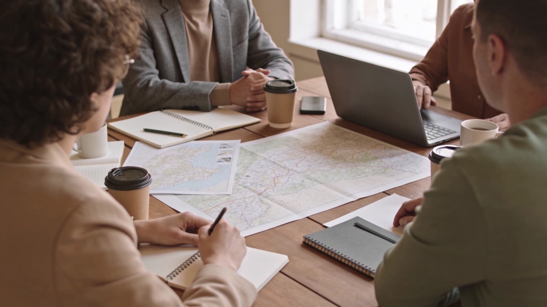 Una squadra al lavoro attorno a un tavolo con mappe, appunti e un portatile